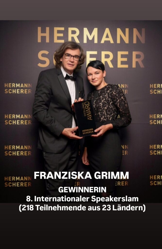 Franziska Grimm Gewinnerin des 8. Internationalen Speaker Days in einem schwarzen Abendkleid. Mit dem Preis in der Hand in Begleitung einer Männlichen Person im Schwarzen Anzug